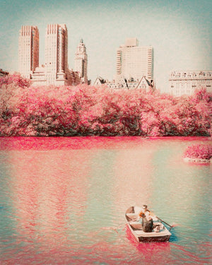 Photograph of a lone rowboat gliding across reflective water, framed by flowering trees and distant city architecture, conveying calm, nostalgia, and quiet romance.